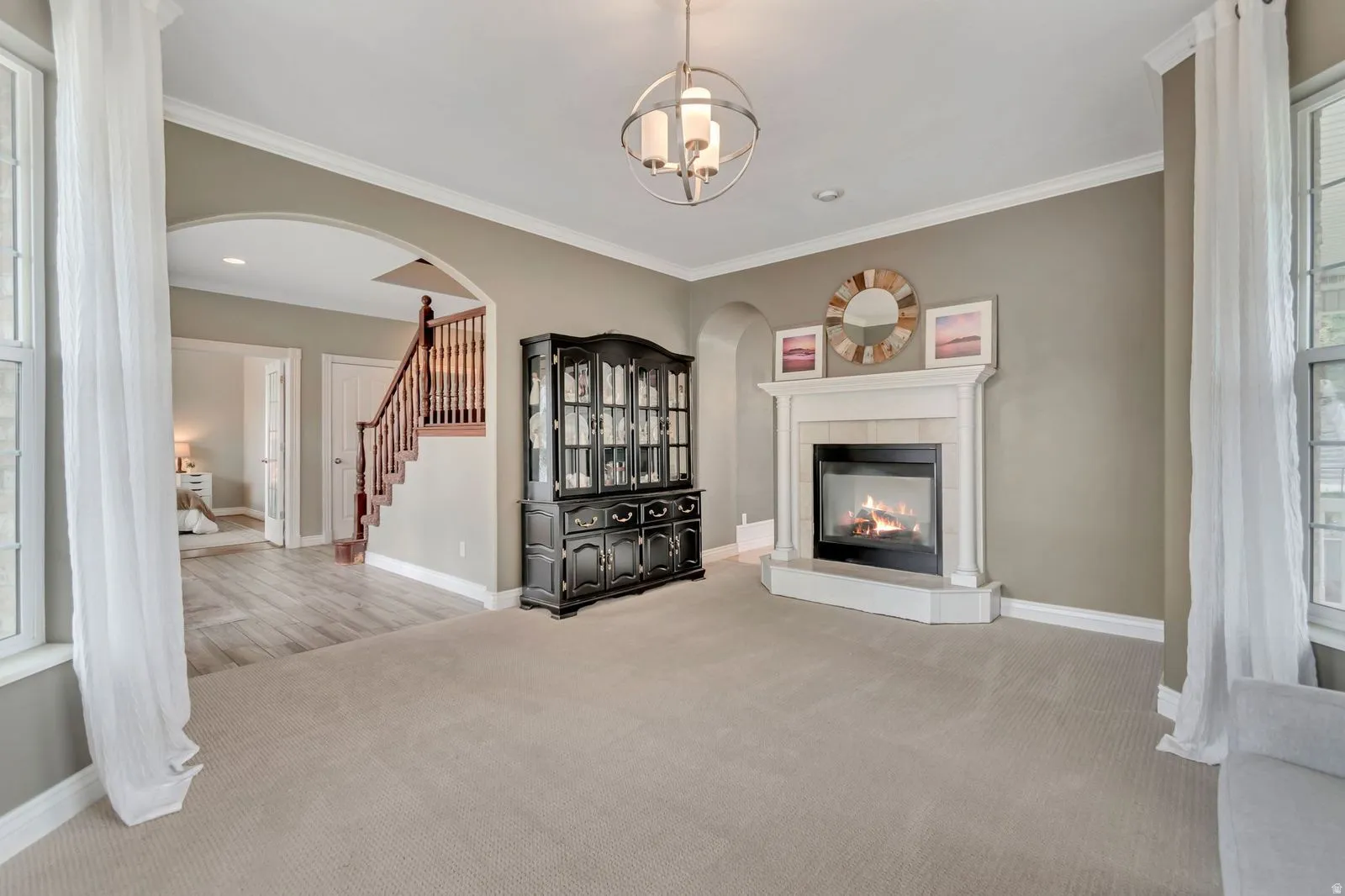 Spacious interior with an architectural archway, a staircase featuring wood newel posts and railings, and a fireplace with a white mantel and hearth