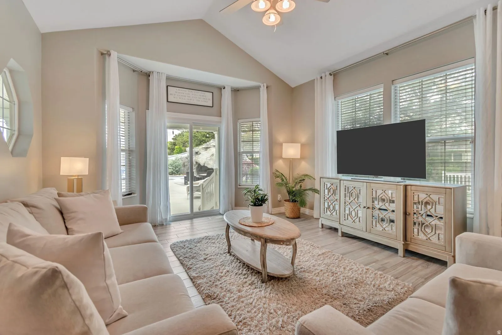 Vaulted ceiling living area featuring light wood-finish flooring, multiple windows with blinds, and a sliding glass door