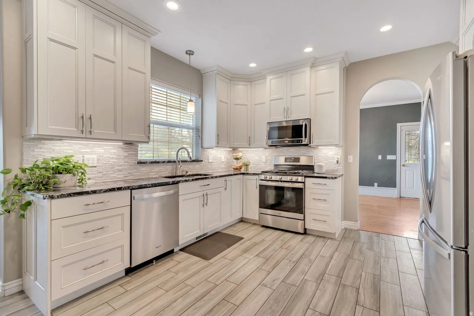 Kitchen featuring light wood-finish flooring, white shaker cabinetry, dark countertops, a mosaic tile backsplash, and stainless steel appliances