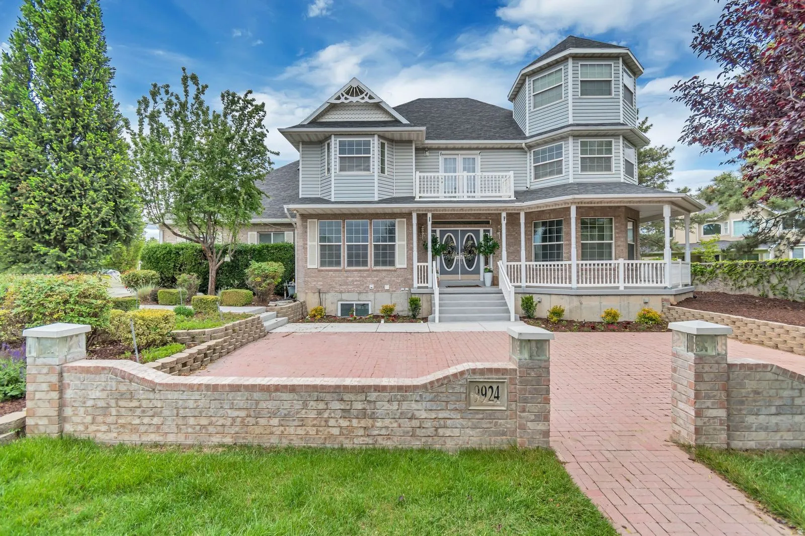 Two-story residence featuring light gray siding with brick accents, a prominent turret, and a covered porch