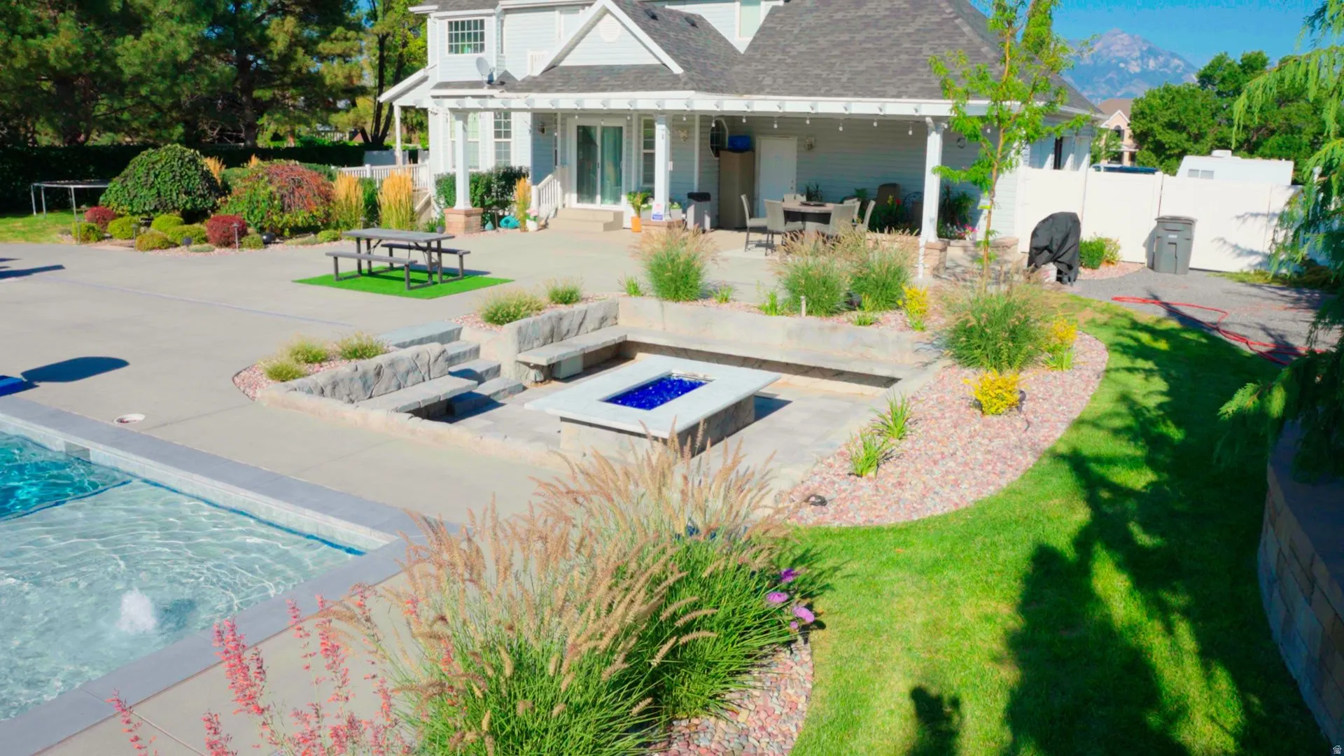 Expansive backyard featuring an in-ground pool with water feature, integrated fire pit with seating, and a large concrete patio