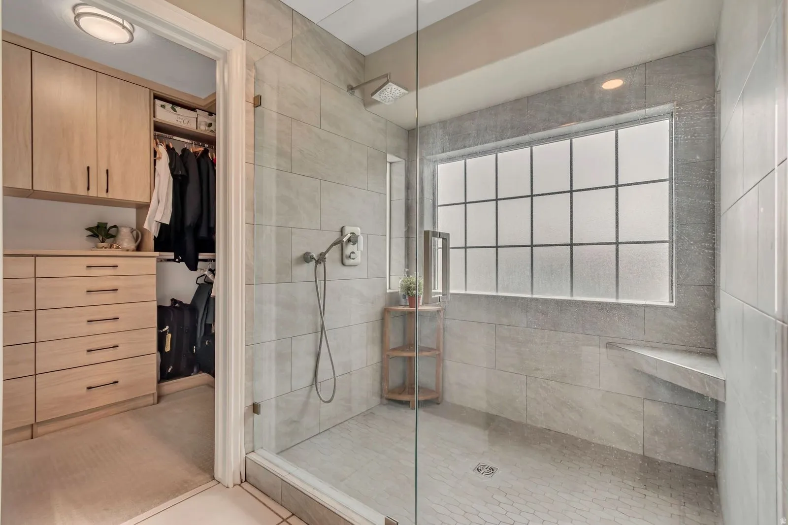 Walk-in shower with full glass enclosure, large format tile walls, a built-in bench, and an opaque window
