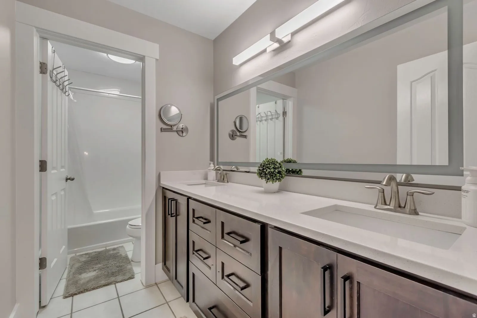 Double vanity featuring dark wood-finish cabinetry, brushed nickel hardware, and a light-toned countertop with integrated sinks