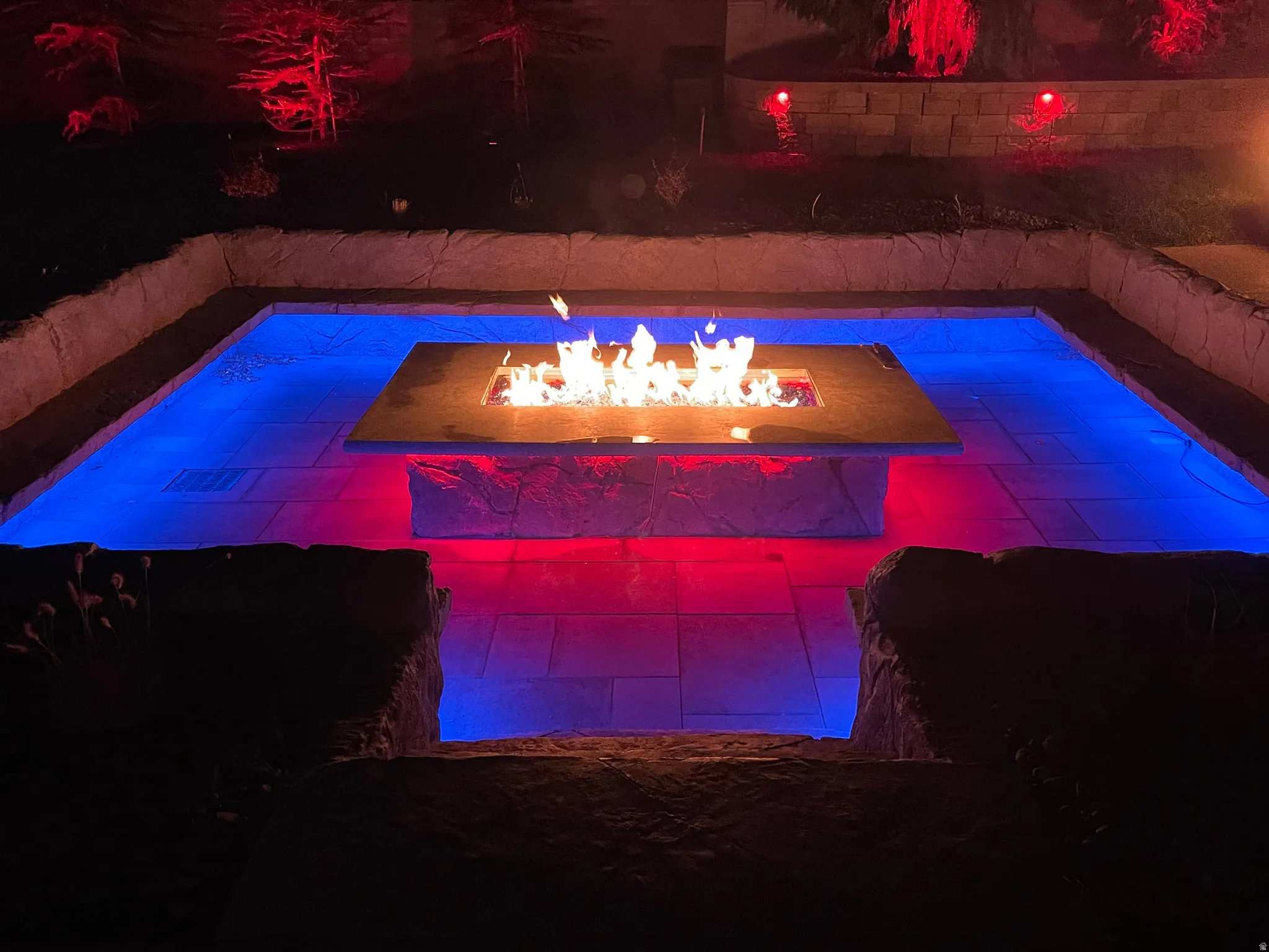Sunken patio featuring a built-in fire pit with stone surround, paver flooring, and integrated ambient lighting