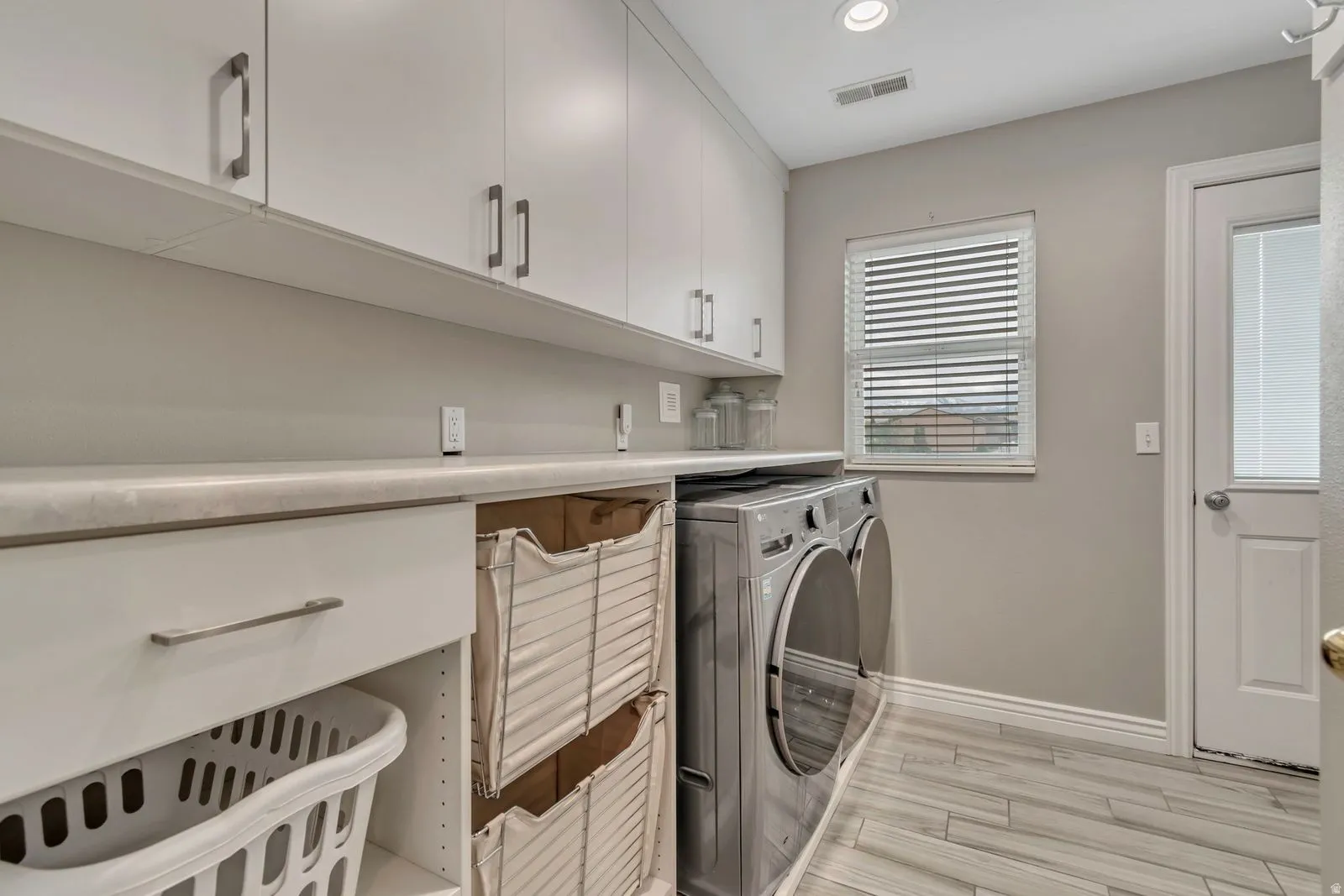 Dedicated laundry room featuring white cabinetry with brushed nickel hardware, a durable countertop, and wood-finish flooring