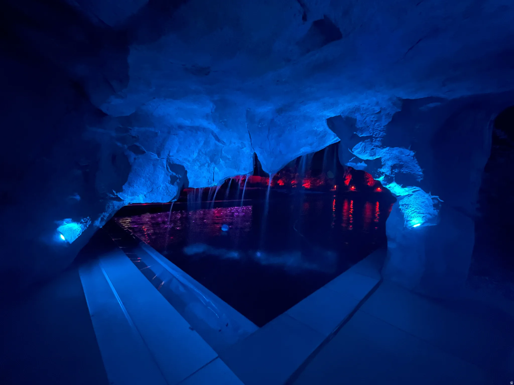 Grotto-style cave pool with blue accent lighting, a waterfall feature, and an entry ramp