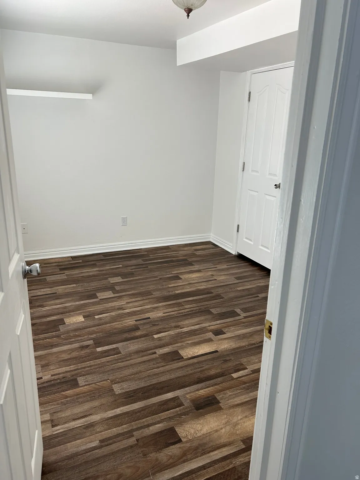 Room with wood-finish flooring, white painted walls, and a white interior door