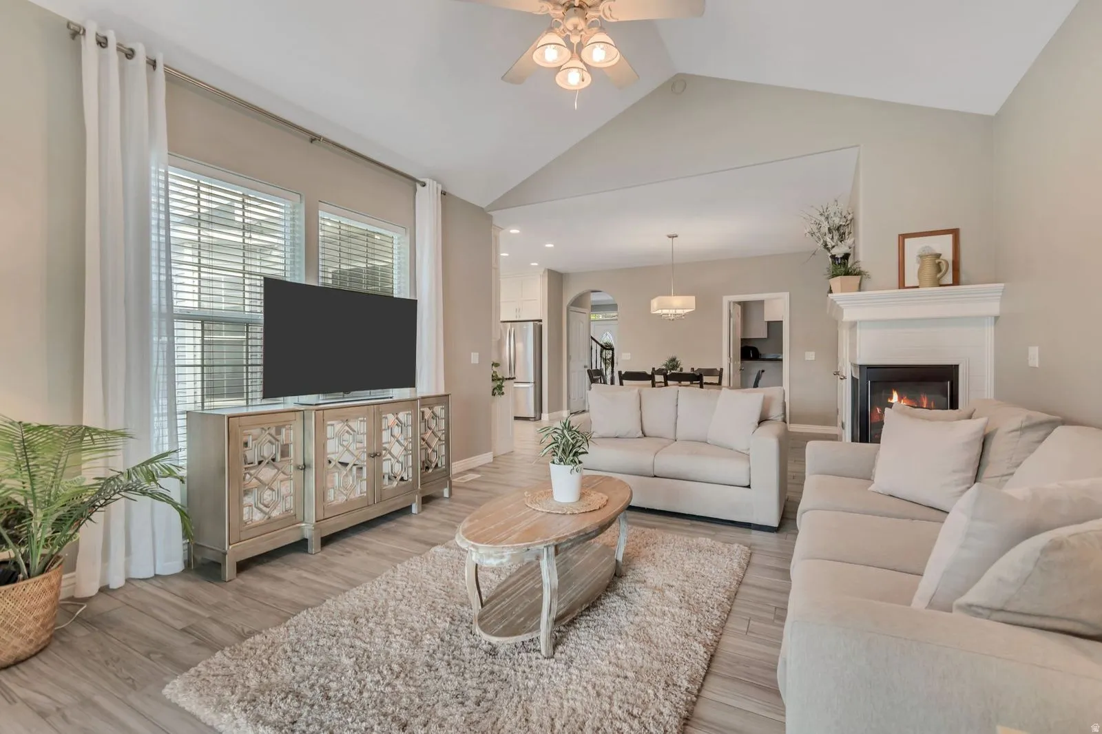 Vaulted ceilings enhance this living space featuring wood-finish flooring, a ceiling fan, and a fireplace with a white mantel