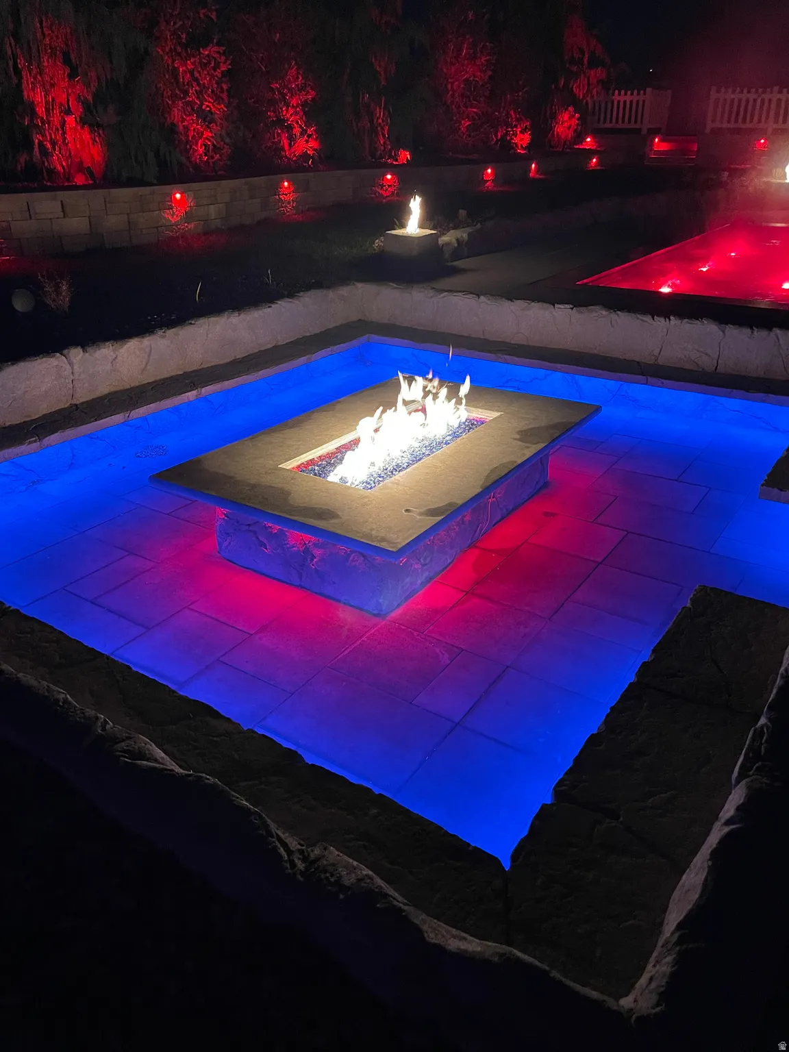Outdoor fire pit featuring a stone surround, integrated seating, and vibrant, adjustable lighting