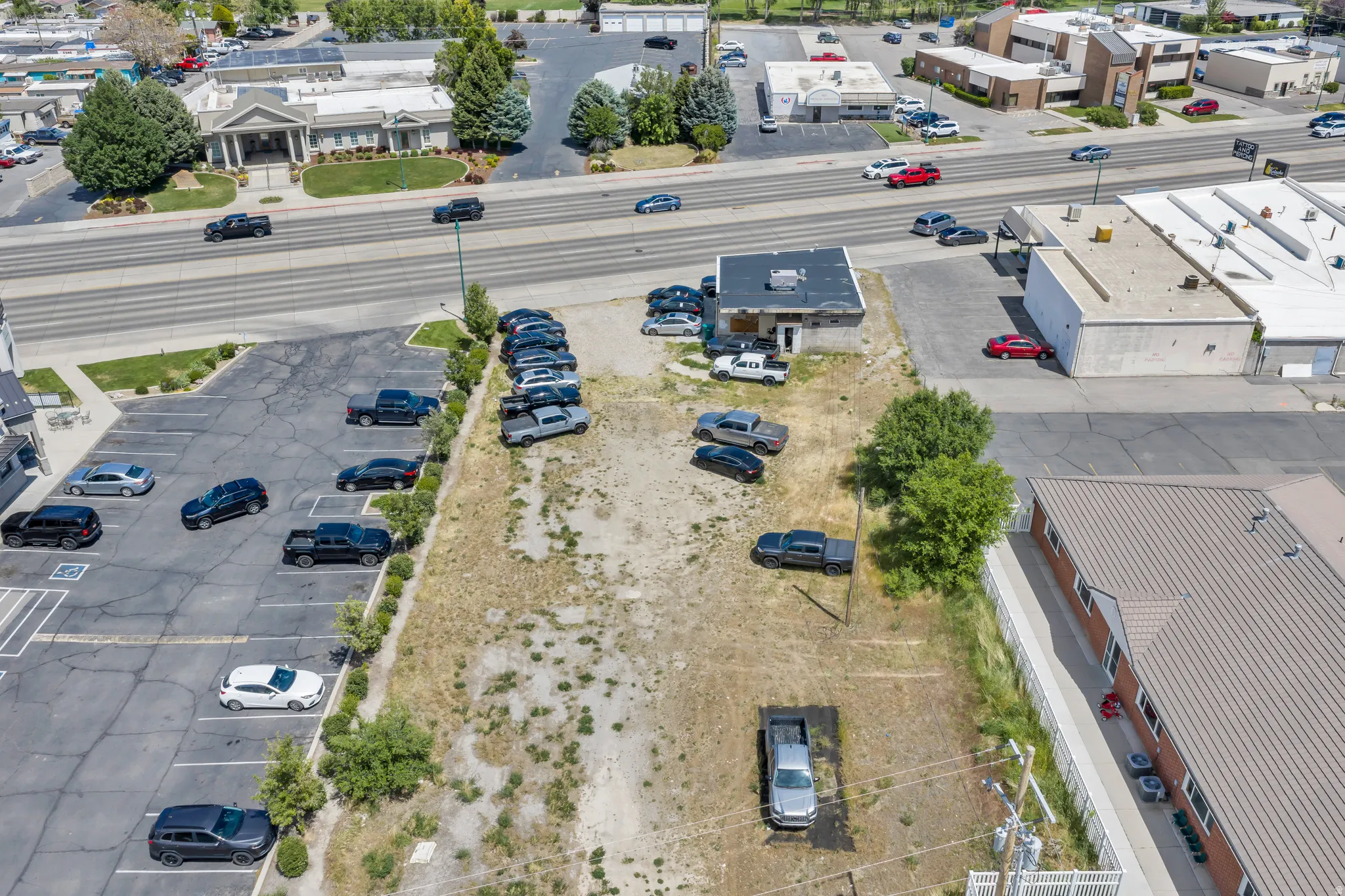 Expansive commercial lot featuring a partial paved parking area, a single-story building with a flat roof, and direct access to a multi-lane roadway
