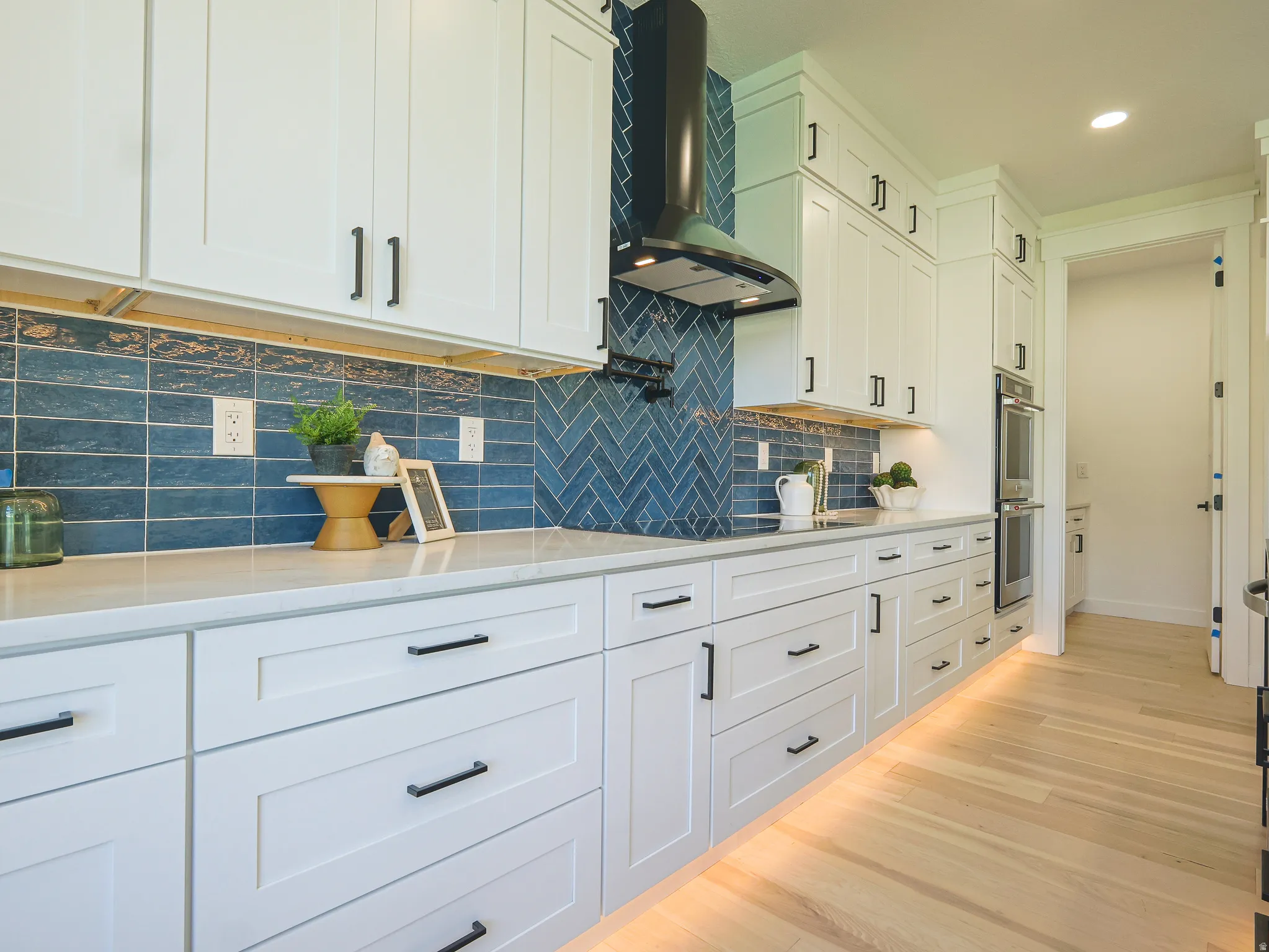 Kitchen featuring white shaker cabinetry, light-toned wood-finish flooring, and a blue tile backsplash in a herringbone pattern above the range