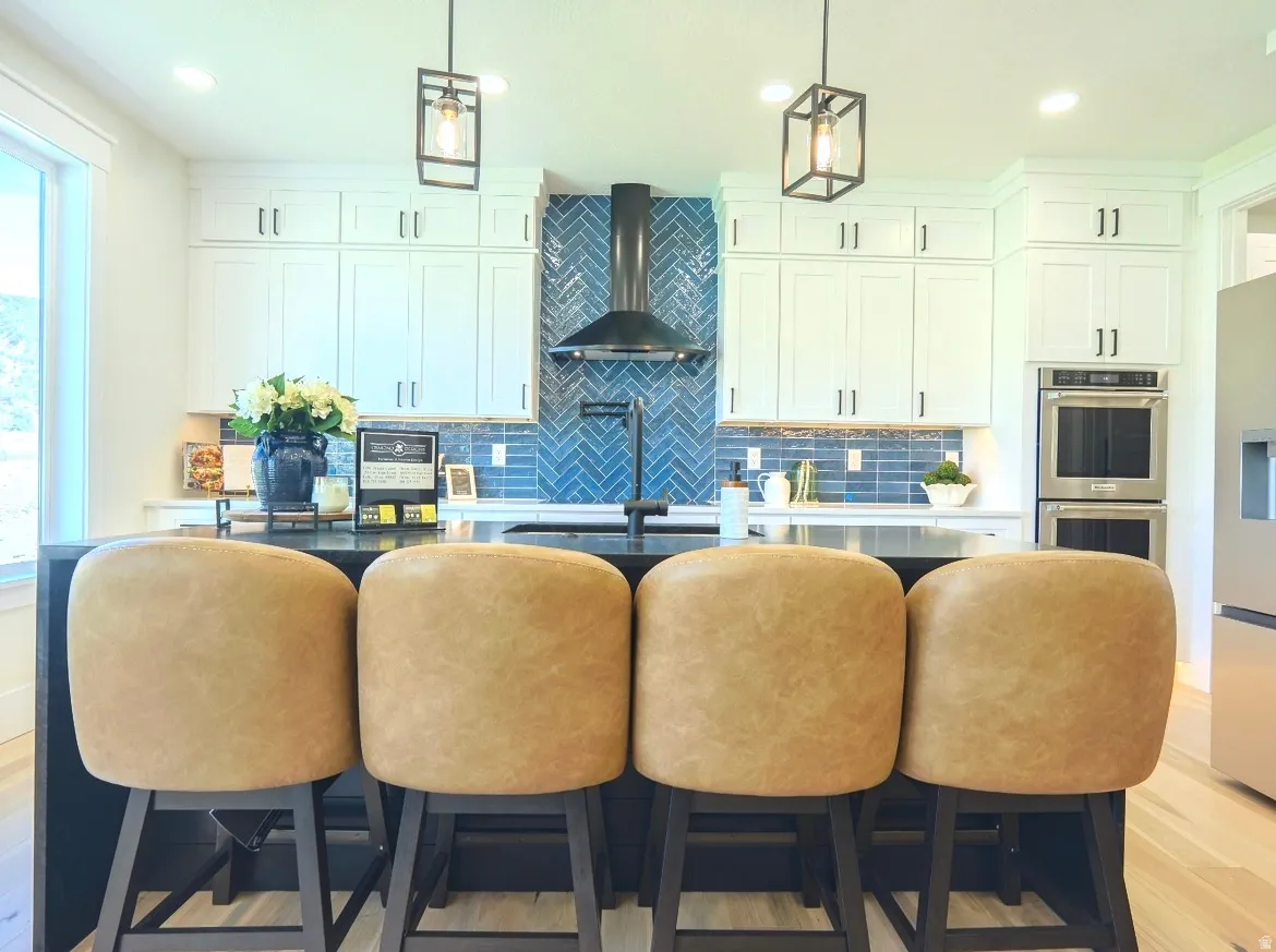 Kitchen featuring a center island, white cabinetry with dark hardware, a blue herringbone tile backsplash, stainless steel double wall ovens, and wood-finish flooring