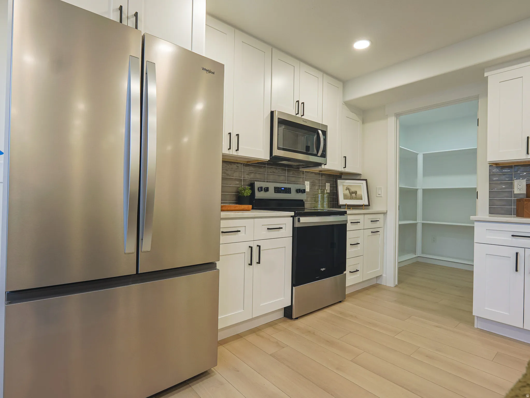 Contemporary kitchen featuring white shaker cabinetry, stainless steel appliances, a dark tile backsplash, and wood-finish flooring
