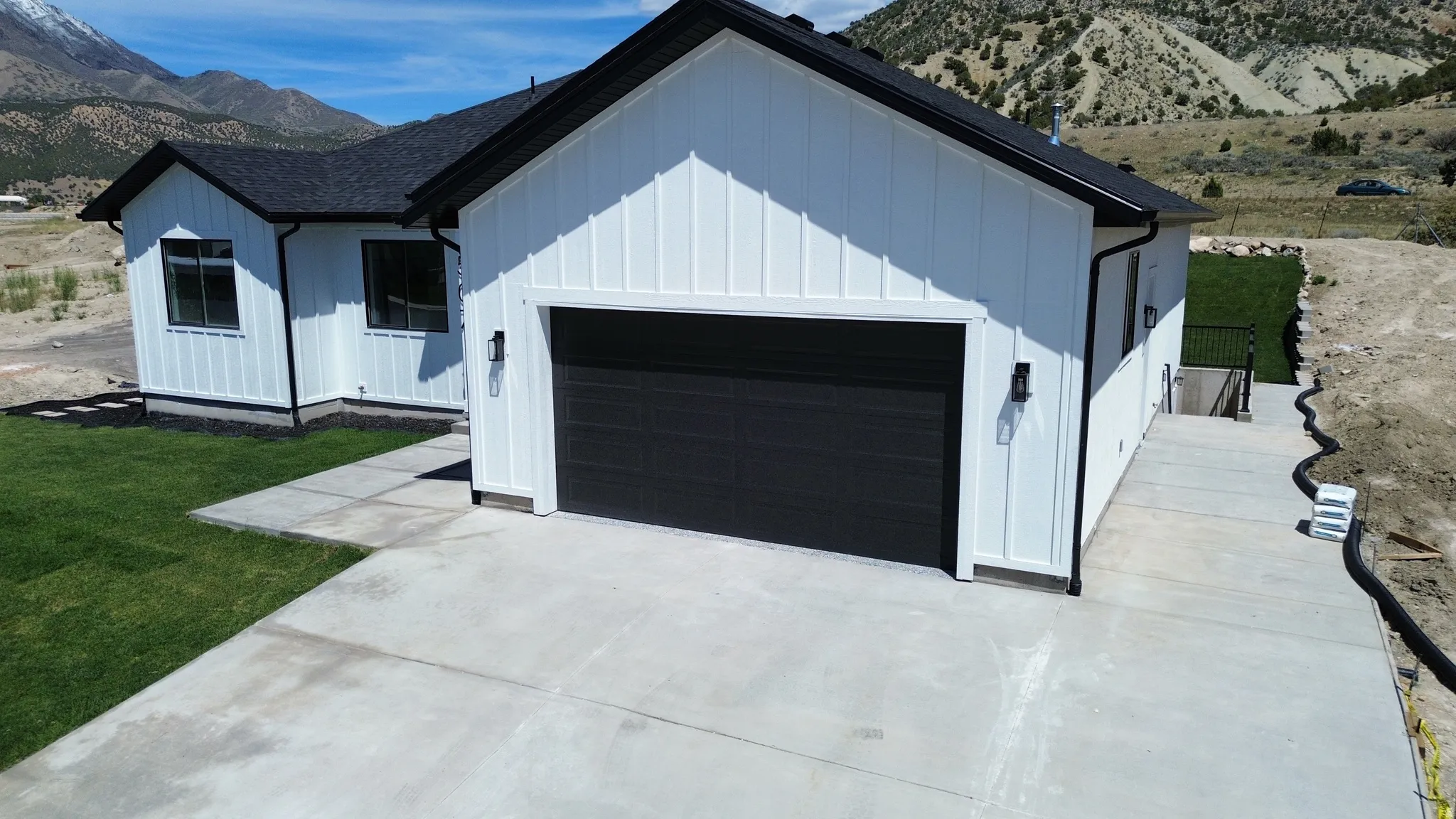 Modern farmhouse-style exterior featuring white board and batten siding, a dark asphalt shingle roof, and a two-car garage with a black door