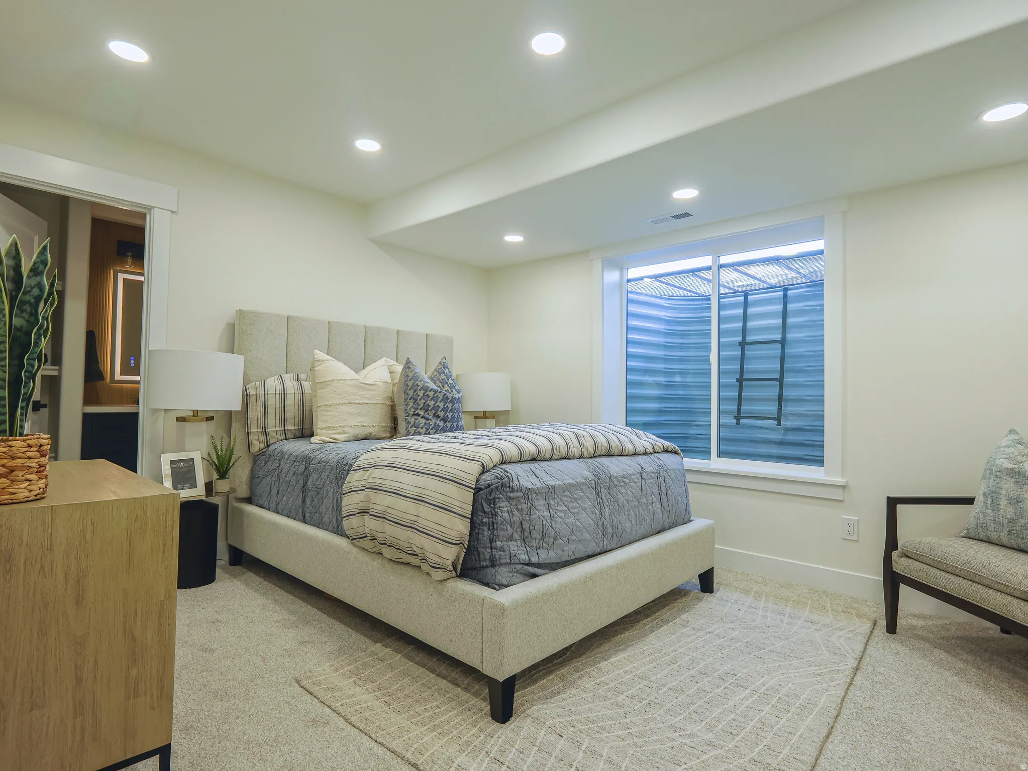 Recessed ceiling lighting illuminates a carpeted room featuring a large egress window with a ladder