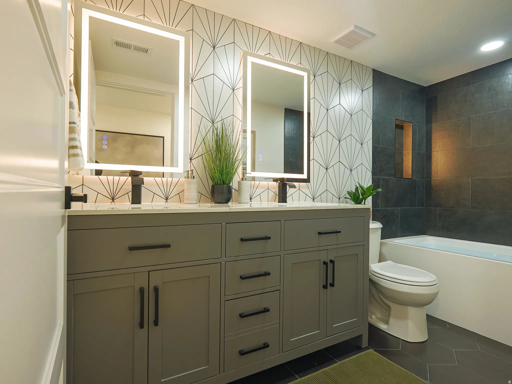 Dual vanity with a stone countertop, illuminated mirrors, and matte black fixtures