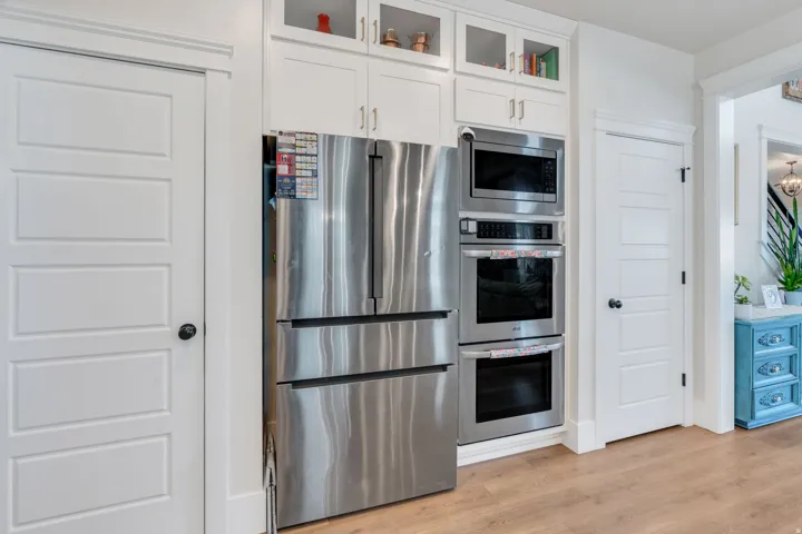 Kitchen with glass insert cabinets, stainless steel appliances, light wood-style flooring, and white cabinets