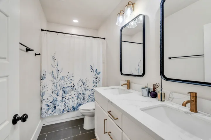 Full bath featuring double vanity, dark tile patterned flooring, shower / bath combo, and recessed lighting