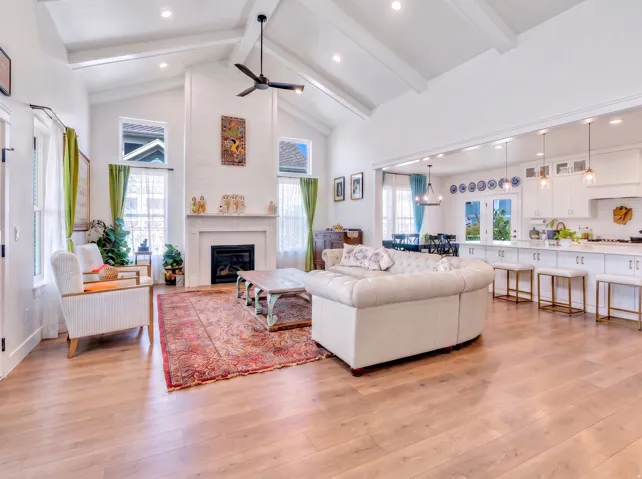 Vaulted ceiling with exposed beams, wood-finish flooring, white shiplap fireplace with mantel, recessed lighting, and kitchen island with pendant lights