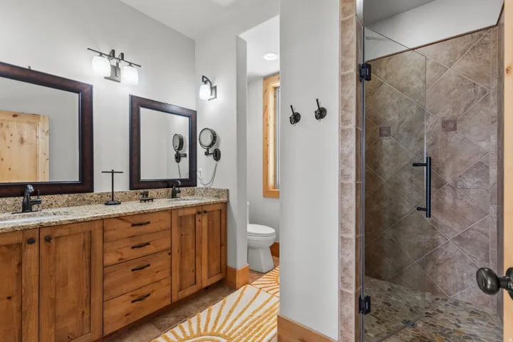 Primary suite with double vanity cherry wood mirrors with wood cabinets and granite countertops, tile flooring.  Beautiful stone tile shower with stone flooring and  glass enclosure.