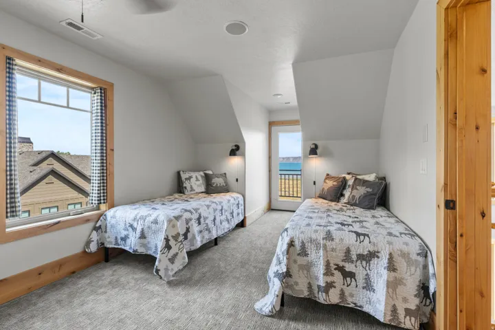 2 of 4 bedrooms, looking at other side of the room from previous photos. Sloped ceiling room featuring light gray carpeting, natural wood trim around the windows and door, and built-in wall sconces