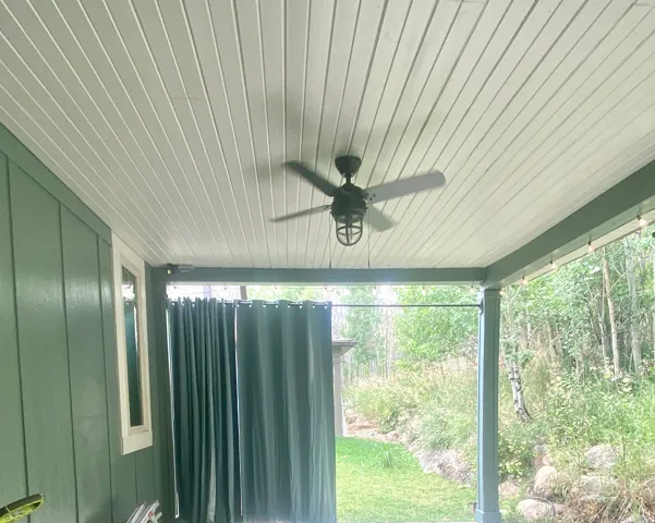 Covered outdoor patio with the white planked ceiling with light/ceiling fan, a green paneled exterior wall, and matching, privacy curtains.