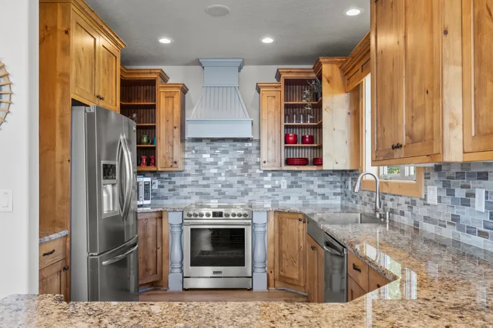Kitchen featuring knotty alder cabinetry, stainless steel appliances, beautiful tile backsplash, polished granite countertops, and recessed ceiling lighting