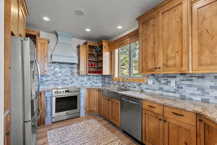 Kitchen featuring knotty alder cabinetry, stainless steel appliances, a multi-tone tile backsplash, and granite countertops.