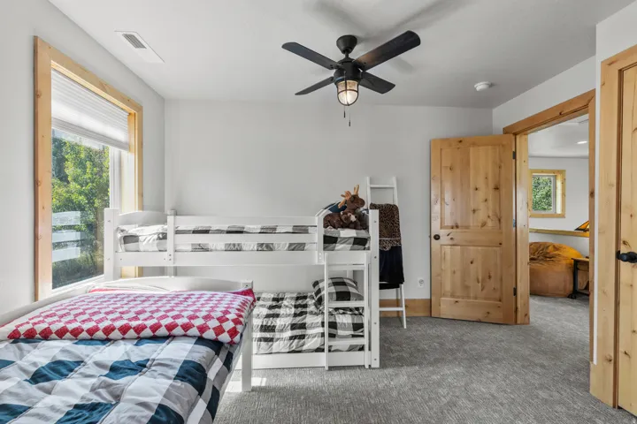 3 of 4 bedrooms featuring light gray carpeting, a large window with natural wood trim, and a black ceiling fan with an integrated light fixture.