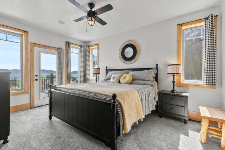 Primary, main floor Bedroom featuring a glass-paned door to an exterior balcony, multiple windows with natural wood trim, and a ceiling fan with integrated lighting.  Gas fireplace offer cozy charm to snuggle in the evenings.