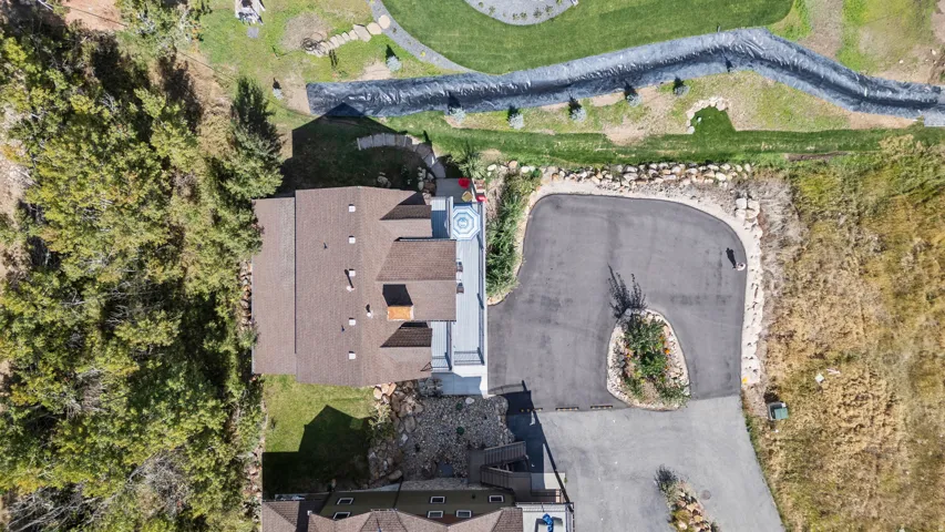 Aerial property overview showcasing a large home with a brown shingle roof, a circular driveway, and an expansive land surrounding, that can't be built on. Back is common area with walking trails. Dead-end street.