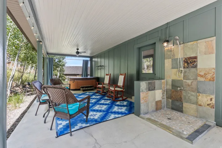 Covered back yard patio featuring an HOT TUB,  outdoor shower with natural stone tile, wood-finish wall paneling, a ceiling fan, and string lighting. Very private with curtain panels.