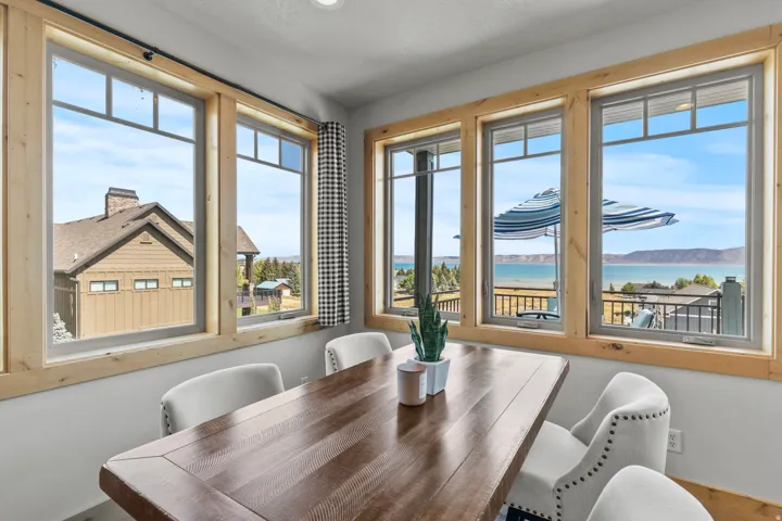 Semi-formal dining area featuring a wood-finish table, upholstered chairs with nailhead trim, and large windows with natural wood trim.  Look at those views. Long deck across the back with door access from great room.