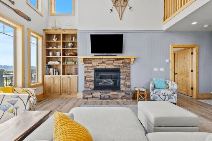 Living room featuring a stacked stone, gas fireplace with a wood mantle, custom built-in shelving, wood trim.