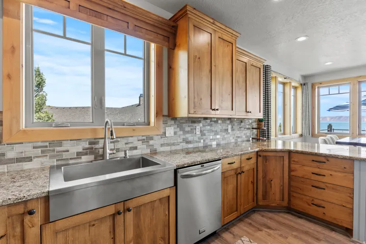Kitchen featuring wood cabinetry, granite countertops, tile backsplash, and a stainless steel farmhouse sink. Bar seating looking over to semi-formal dining.