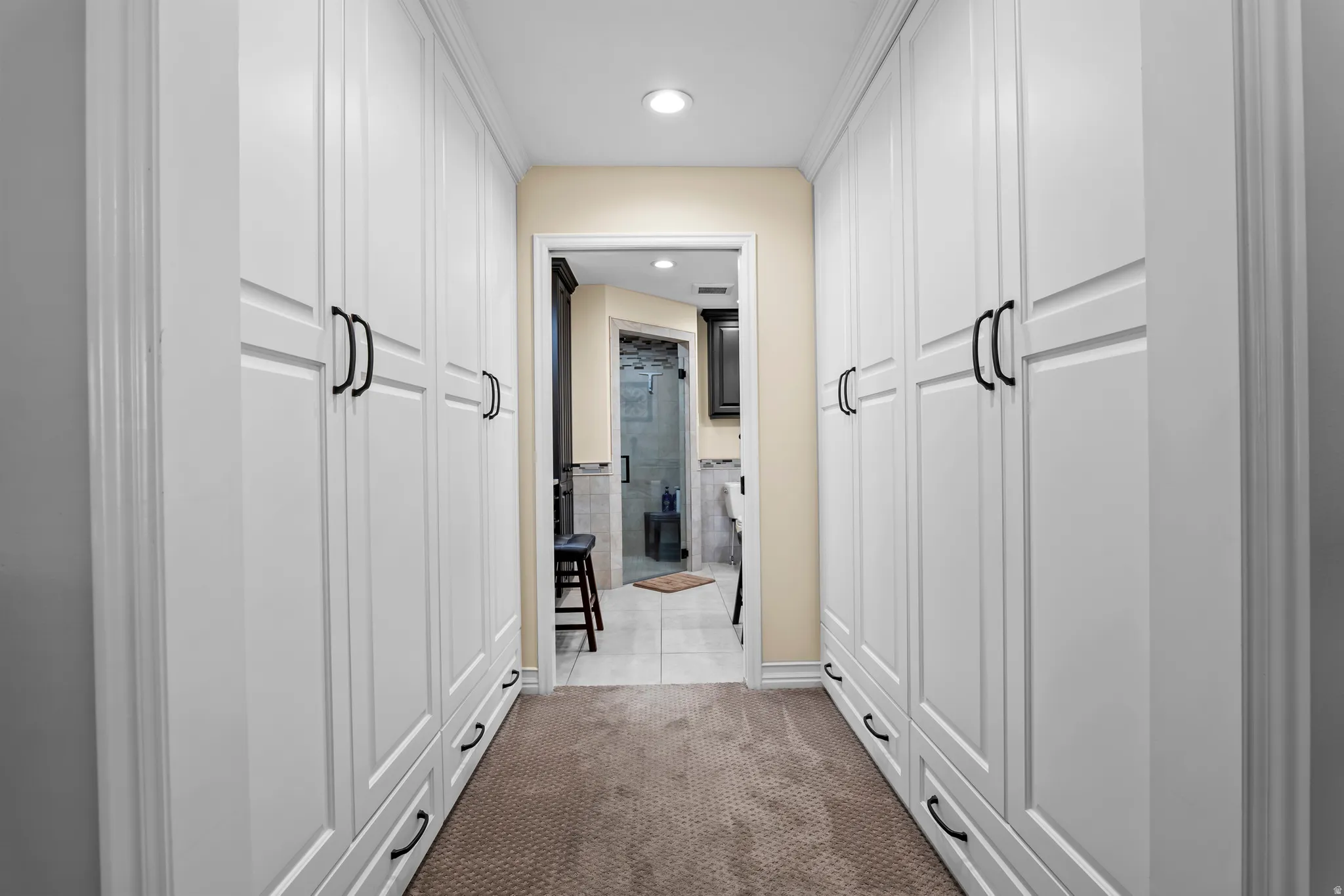 Hallway featuring extensive built-in white cabinetry with black hardware, recessed lighting, and neutral-toned carpeting
