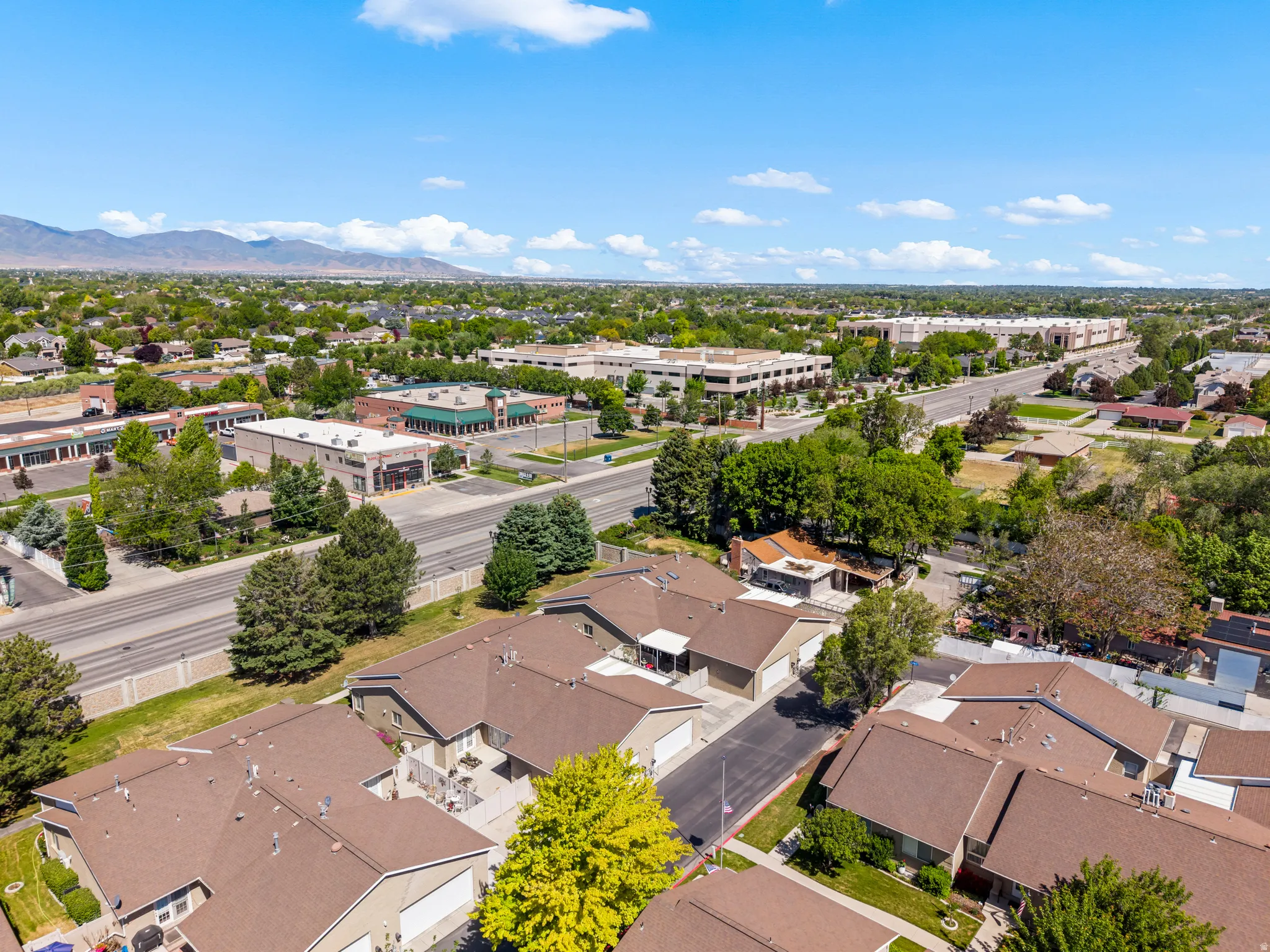 Aerial perspective showcasing residential rooftops with mature trees, commercial buildings, and a distant mountain range under a clear sky