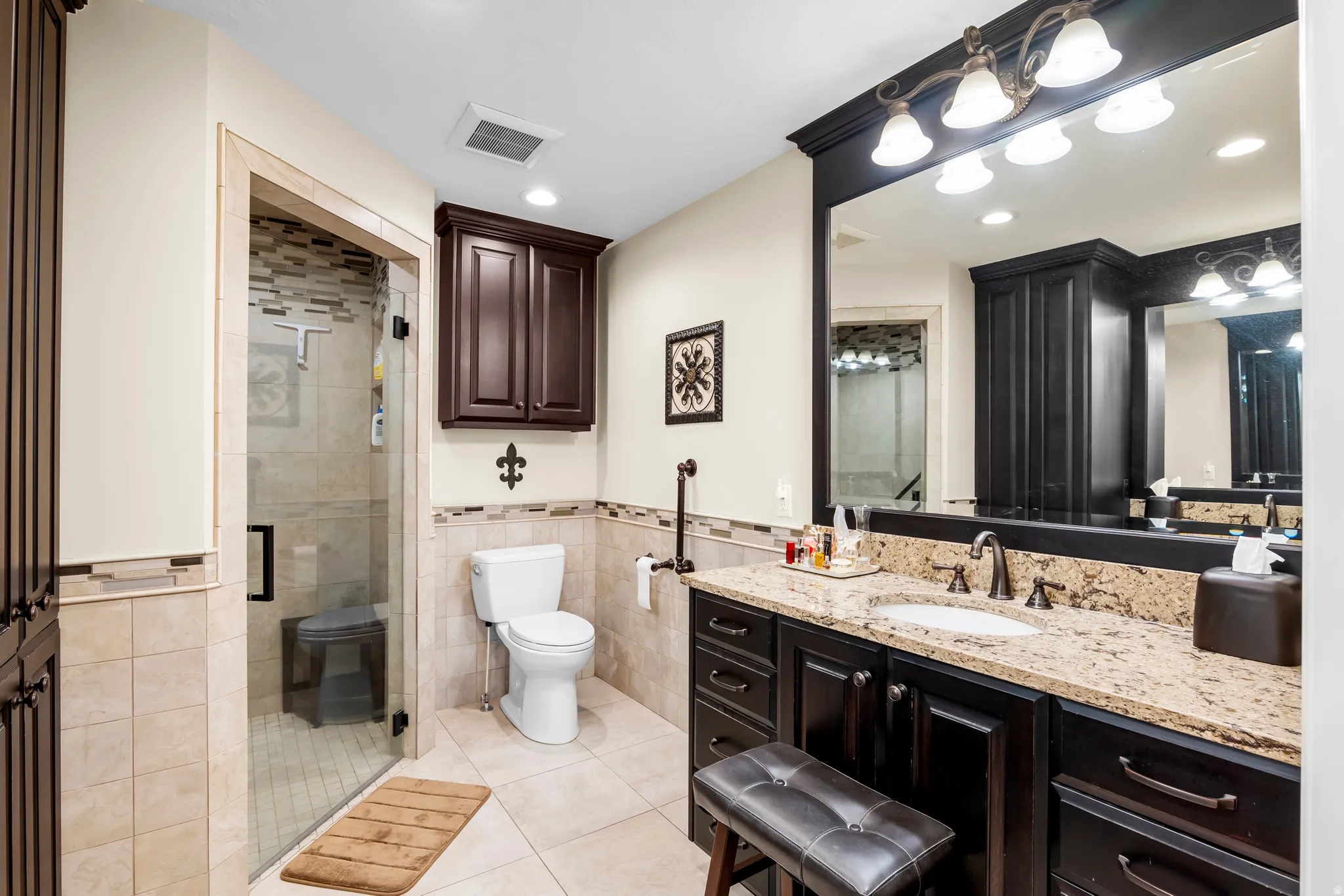 Bathroom featuring a glass-enclosed shower, a vanity with stone countertop, dark wood cabinetry, a built-in wall mirror, and recessed lighting