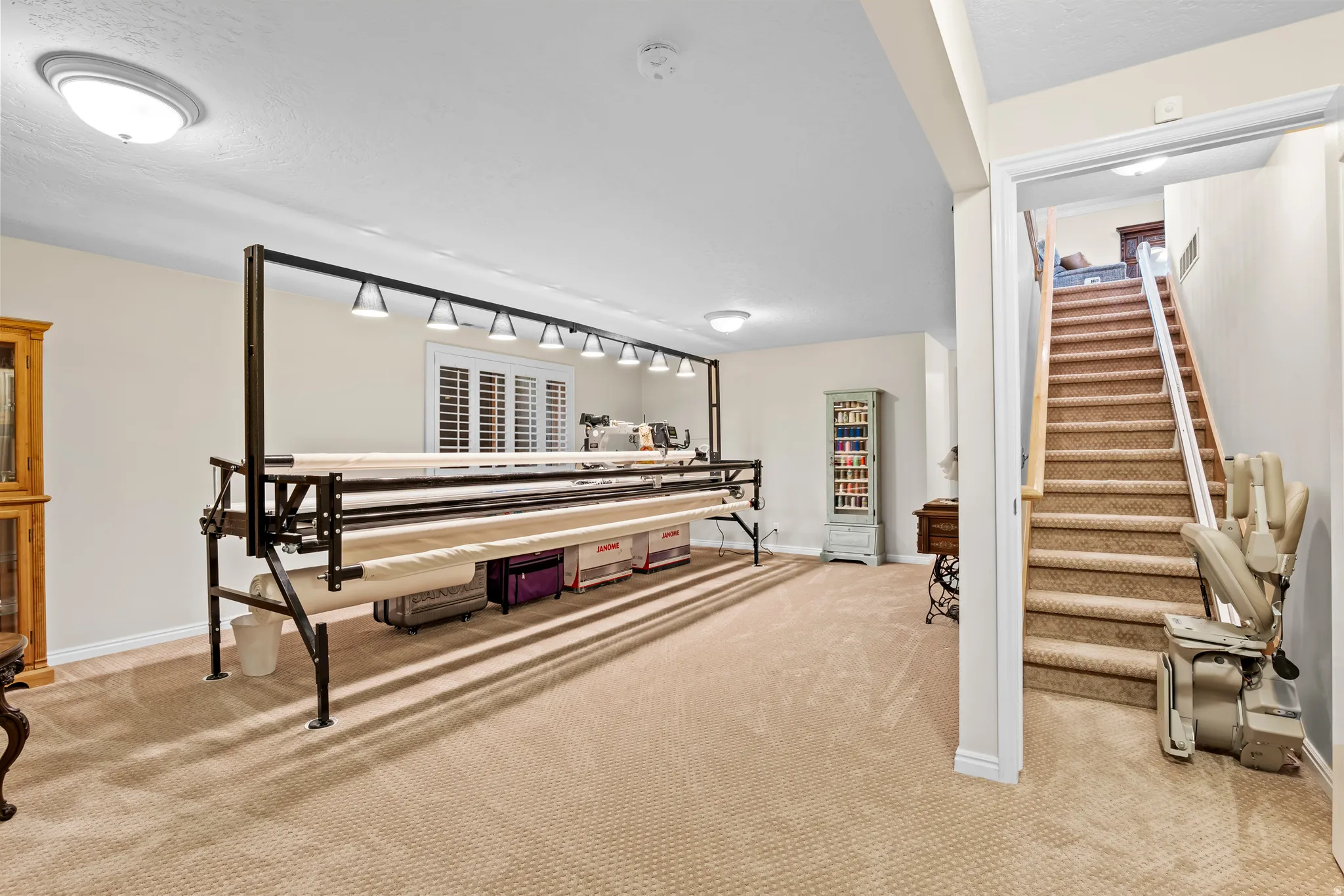 Spacious carpeted room with multiple ceiling lights and a window with plantation shutters