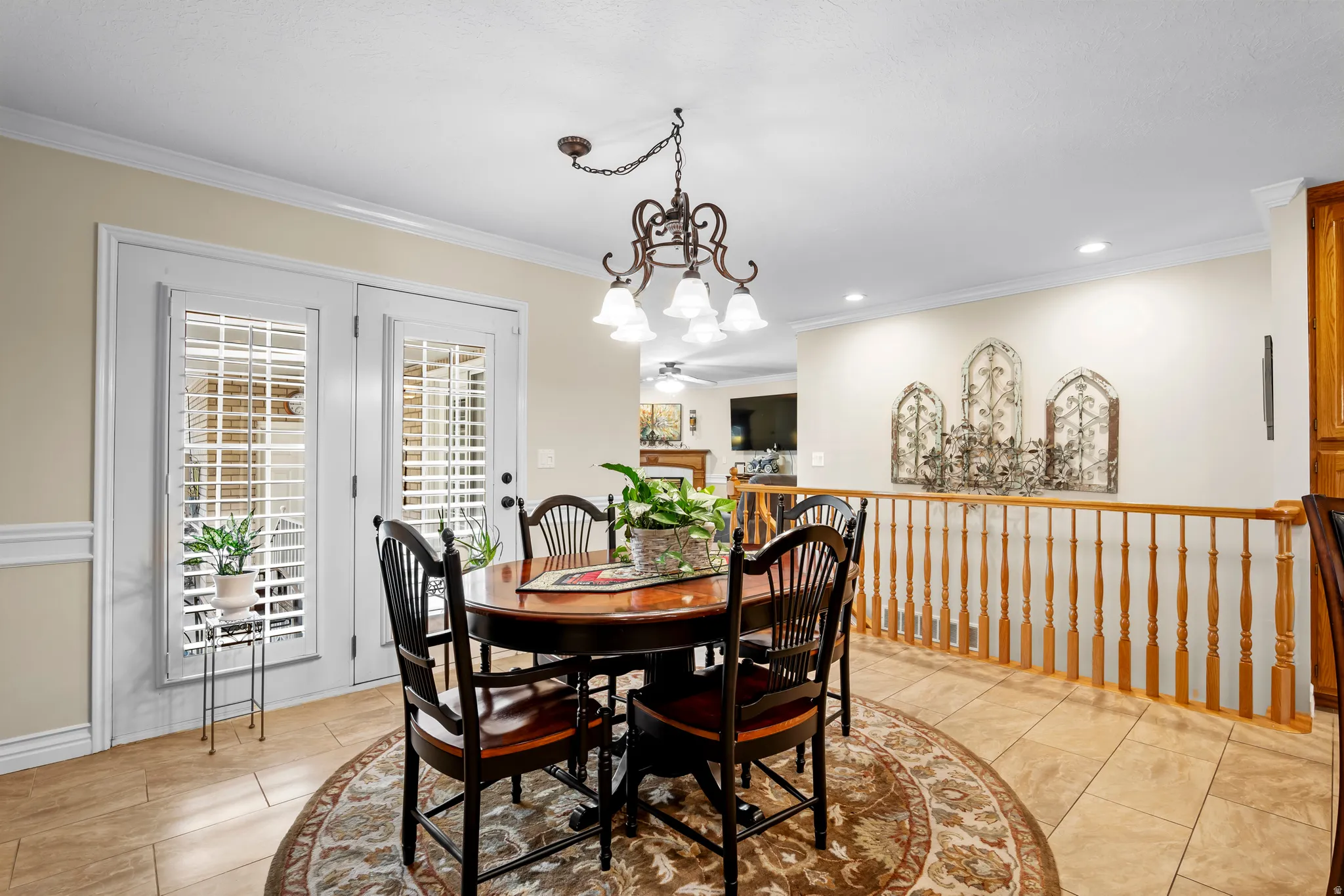 Dining area featuring tile flooring, a decorative chandelier, white crown molding, and double glass-paned doors with internal white shutters