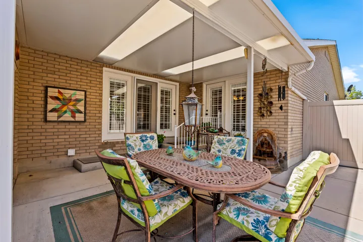 Covered patio featuring a cast iron style table and chairs, brick exterior, concrete flooring, and a decorative privacy fence