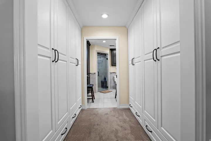 Hallway featuring extensive built-in white cabinetry with black hardware, recessed lighting, and neutral-toned carpeting