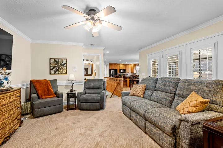 Spacious living area featuring neutral carpeting, crown molding, and a ceiling fan with integrated lighting