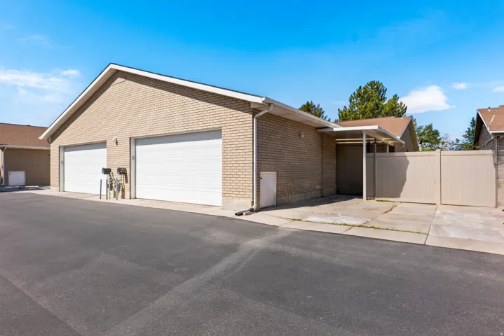 Brick exterior featuring two white garage doors, a covered carport, paved driveway, and perimeter fencing