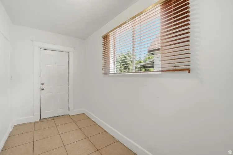 Entry area featuring tiled flooring, a paneled door, a horizontal window with wooden blinds, and white painted walls