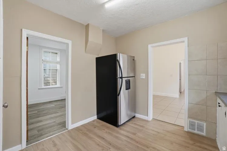 Kitchen area featuring wood-finish flooring, a stainless steel refrigerator, neutral wall paint, and a tiled backsplash