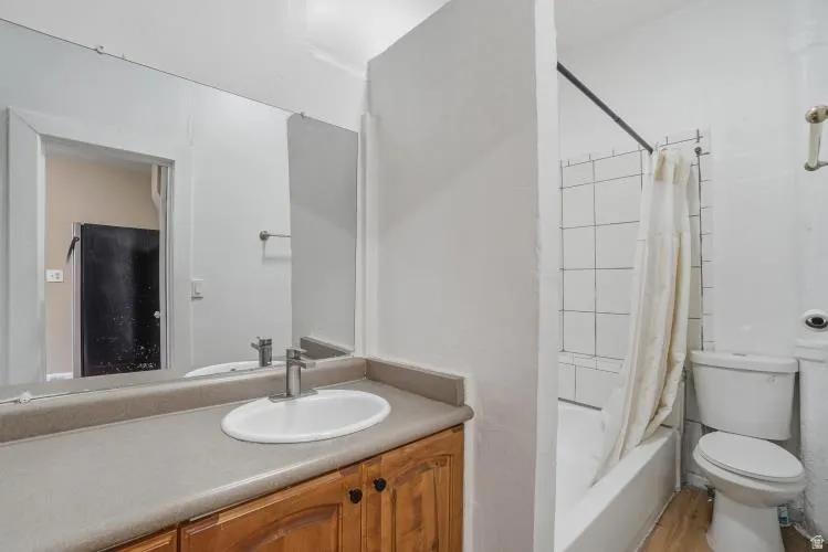Bathroom featuring a vanity with wood cabinetry and a neutral countertop, an integrated sink with a chrome faucet, a large wall-mounted mirror, and a white tiled shower/tub combination