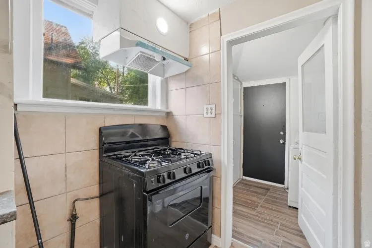 Kitchen area featuring a black gas range, tile backsplash, and overhead range hood