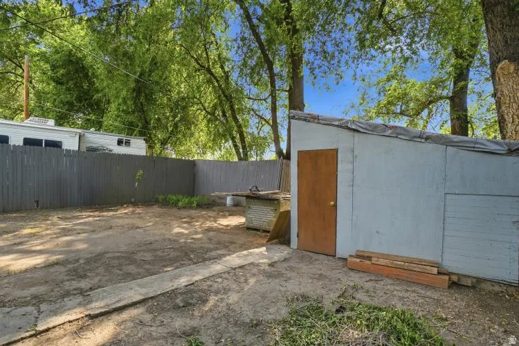 Spacious backyard featuring a gray wood fence, mature trees, and a storage shed with a wood door