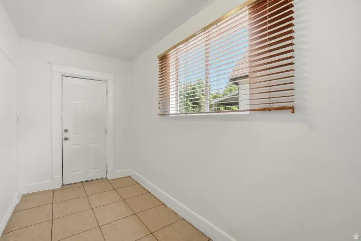 Entry area featuring tiled flooring, a paneled door, a horizontal window with wooden blinds, and white painted walls